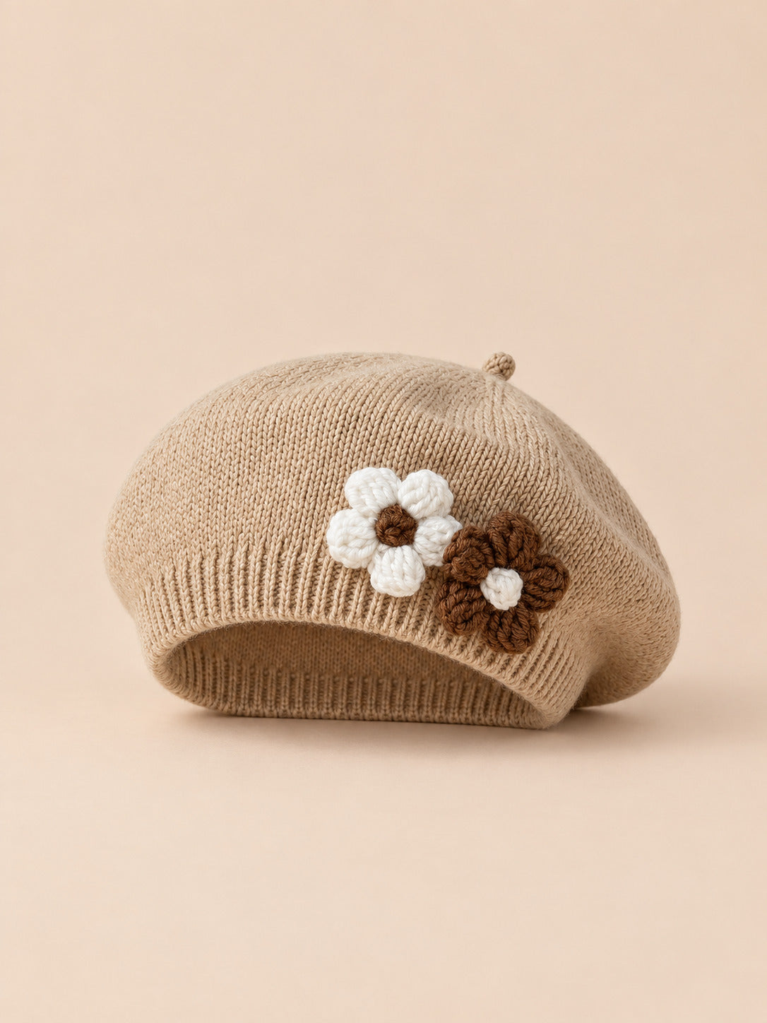 Béret bébé fille Café à fleurs en relief au crochet, vue de face sur fond pêche sable